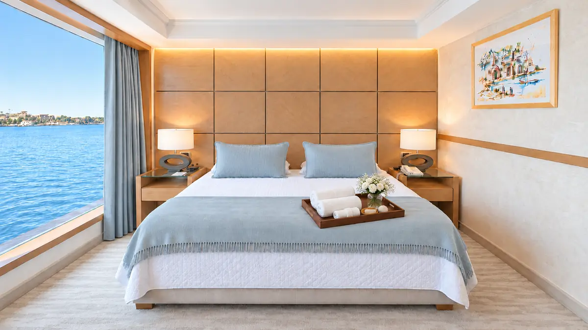Amwaj Boat Renovation – Cabin with pale blue throw, towels on a tray and a river view