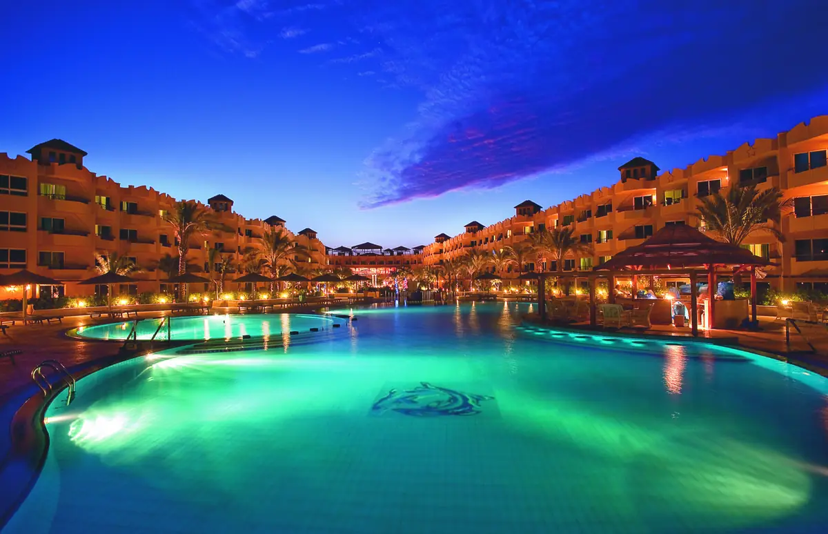 Amwaj Soma Hotel & Spa – Türkis leuchtender Lagunenpool in der Dämmerung mit Delfinmosaik und beleuchteten Flügeln