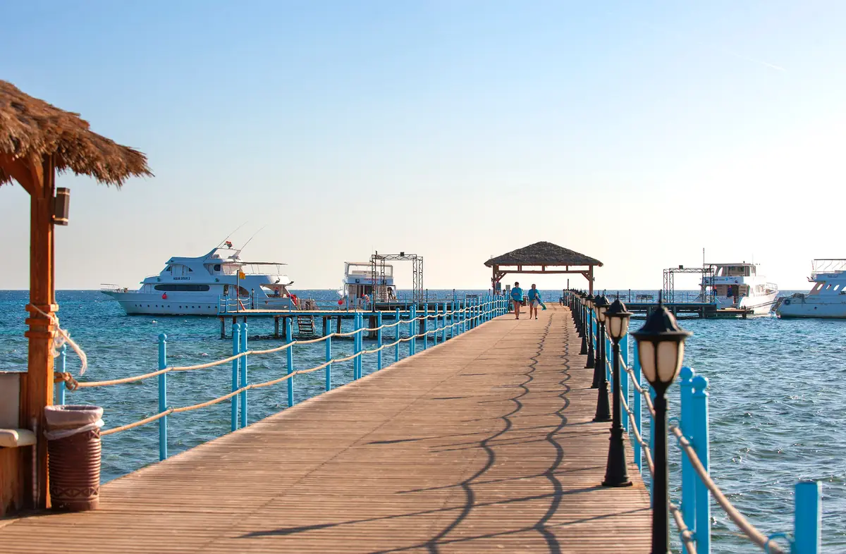Amwaj Soma Hotel & Spa – Holzsteg mit blauem Seilgeländer und Laternen, der zu vertäuten Booten führt