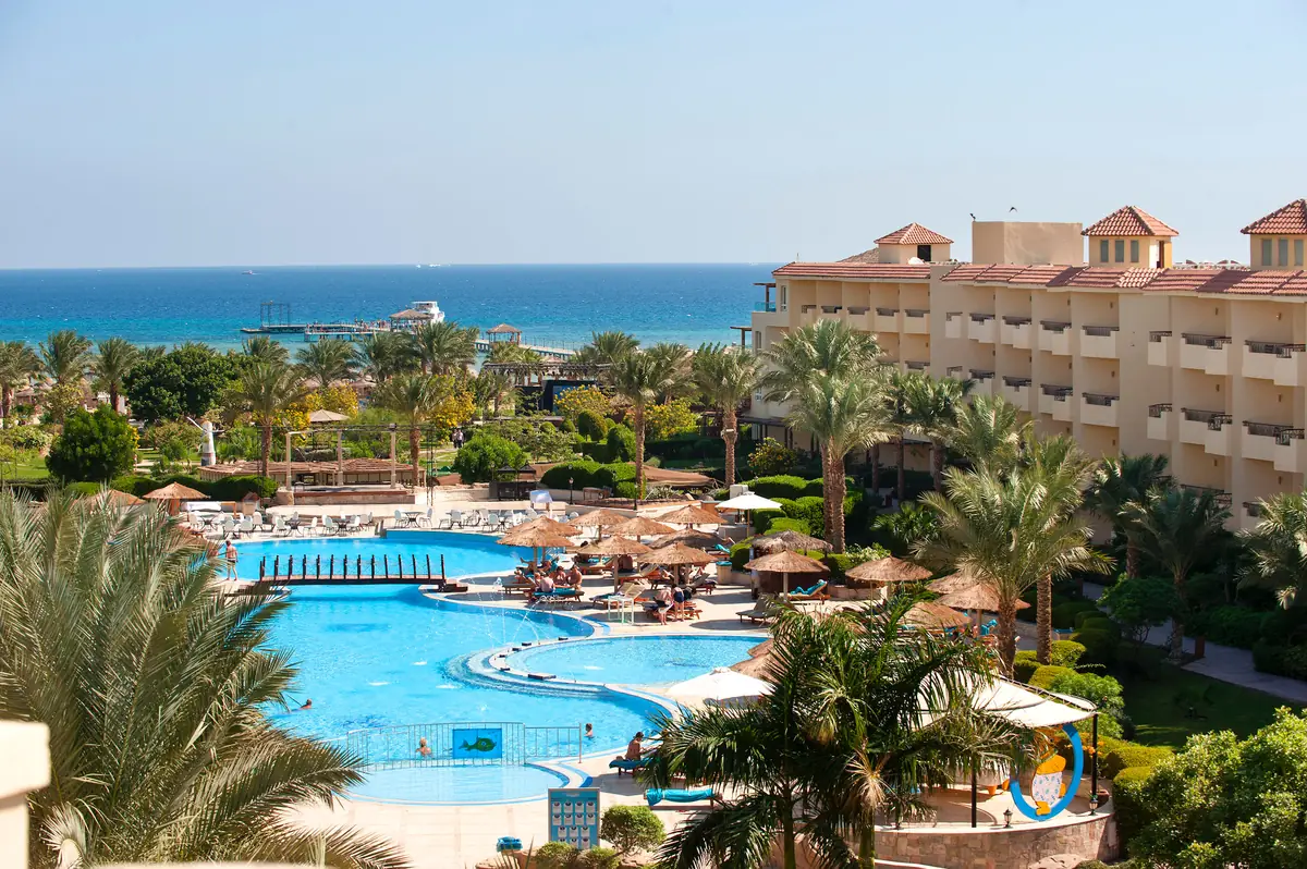 Amwaj Soma Hotel & Spa – Pools und Palmengärten unter einem gestuften Terrakotta-Flügel, dahinter das Meer