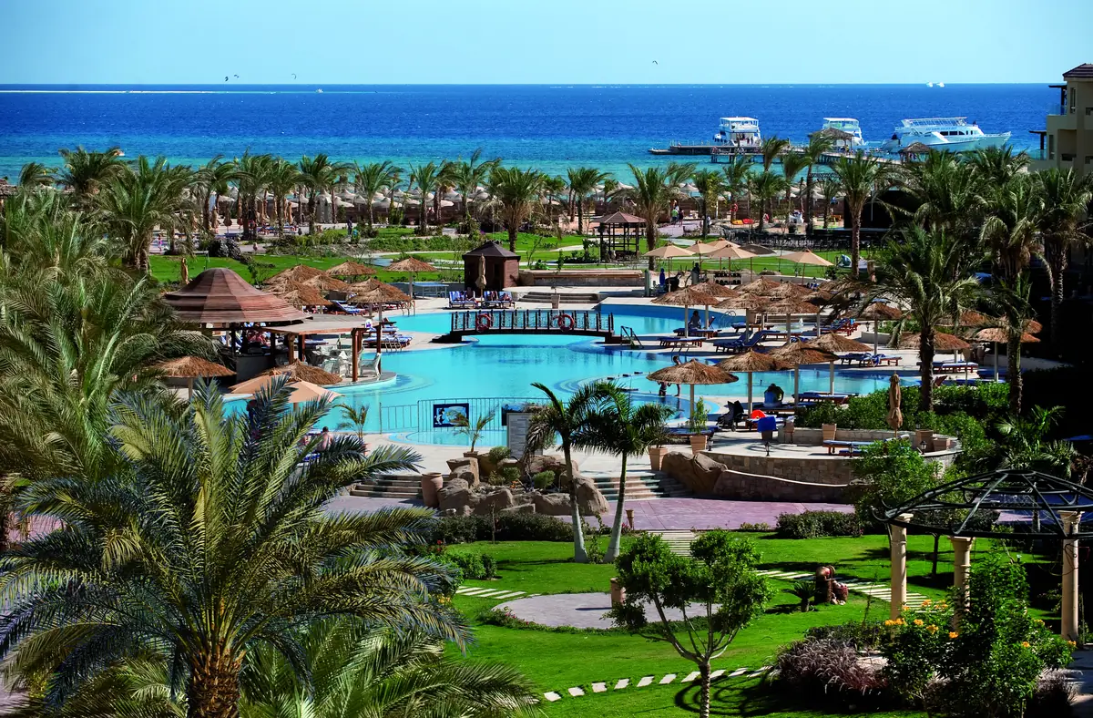 Amwaj Soma Hotel & Spa – Palmengärten und Rasenflächen, die zu den Pools abfallen, mit Booten vor der Küste