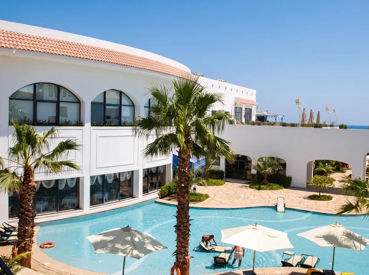 Blue Bay Resort Thalassotherapy Spa – واجهة بيضاء مقوسة ونخيل حول مسبح بمظلات