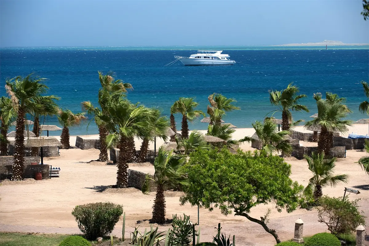 Lotus Bay Resort Renovation – Palm-studded beach with parasols and a moored yacht on the deep blue sea