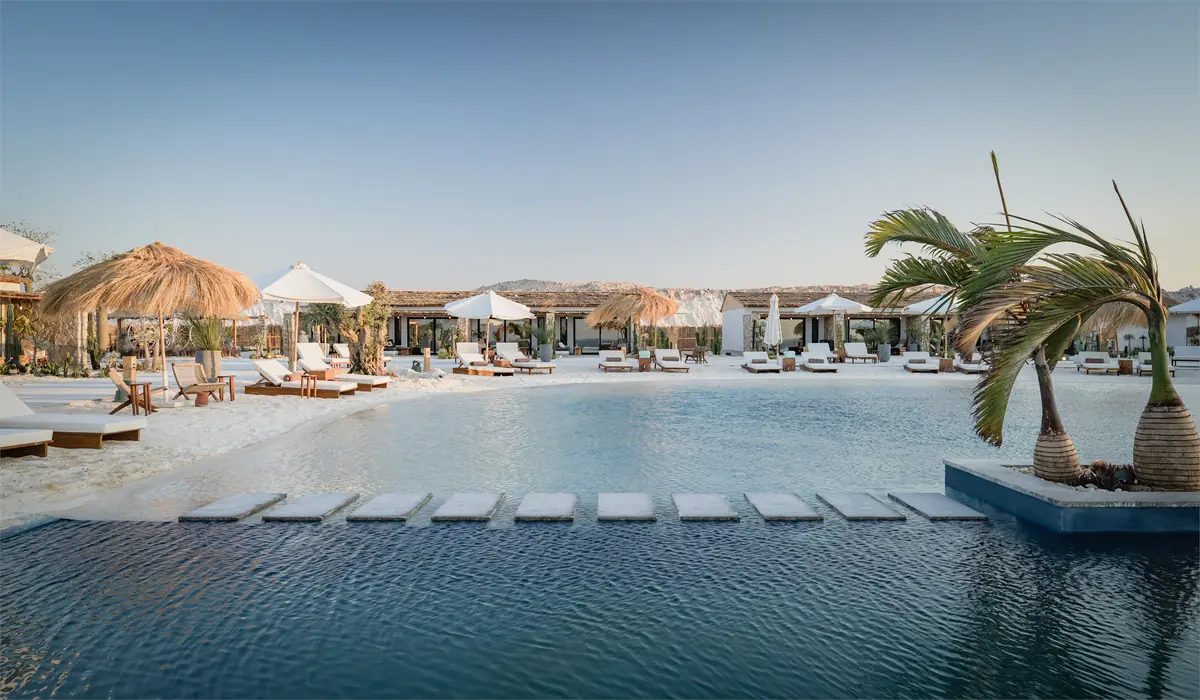 Marmarica Boutique cabanas – Long pool crossed by stepping stones, with thatched parasols and cabanas beyond