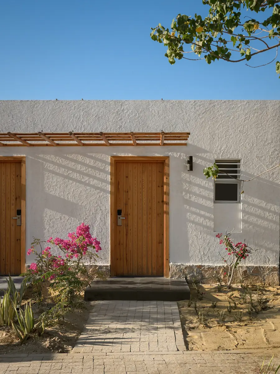 Marmarica Boutique cabanas – Weiß strukturierte Cabana-Wand mit Holztüren, Pergola und Bougainvillea