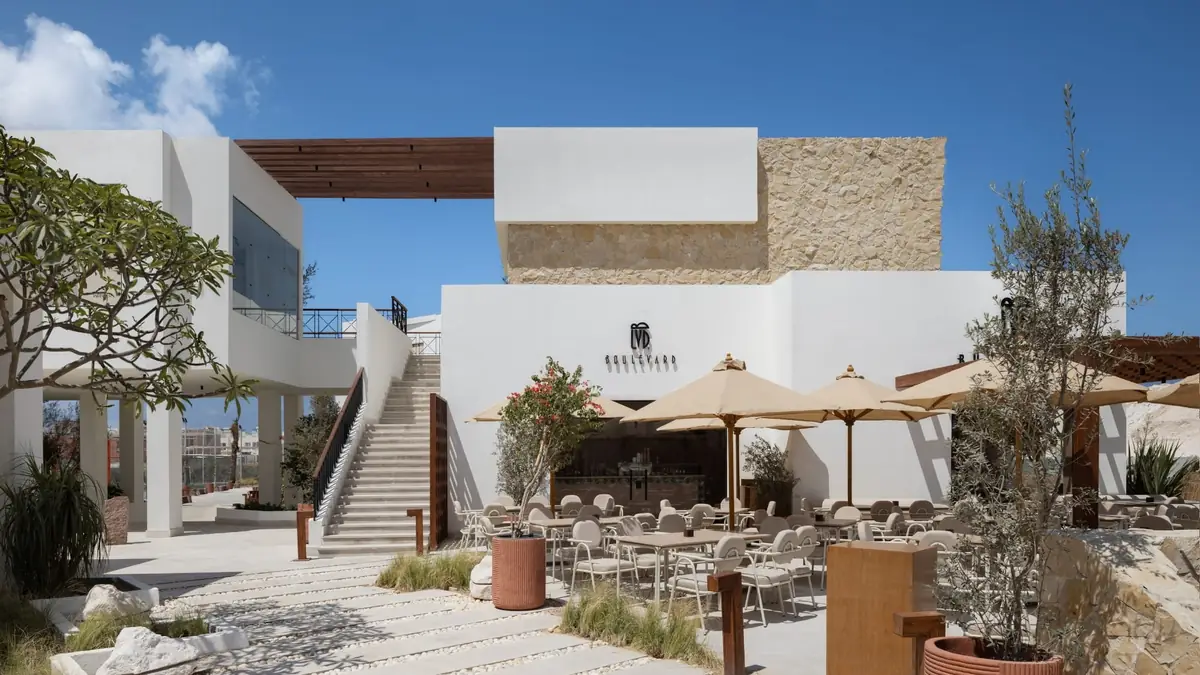 Masyaf Ras Al-Hekma – Restaurantterrasse mit Sonnenschirmen unter einem steinverkleideten Baukörper und offener Treppe