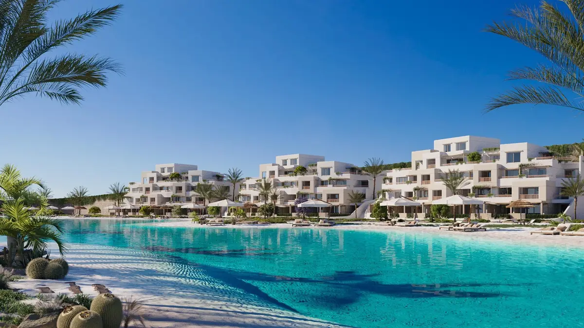 Oyster at Masyaf – بحيرة فيروزية يحيط بها النخيل والصبار أمام مبانٍ سكنية بيضاء متدرجة