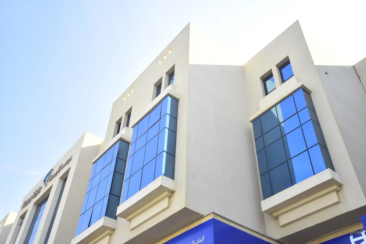 Prima Vista – Medical Office & Commercial Mall – منظر إلى الأعلى لنوافذ بارزة من الزجاج الأزرق في واجهة كريمية دافئة مع فتحات صغيرة في الدروة