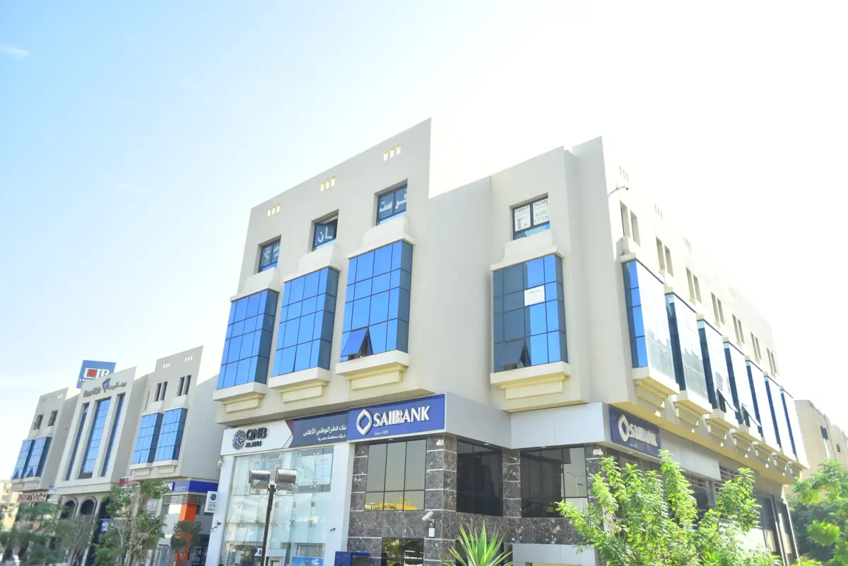 Prima Vista – Medical Office & Commercial Mall – منظر أوسع لزاوية المبنى مع المباني المجاورة وأشجار الشارع تحت سماء ساطعة