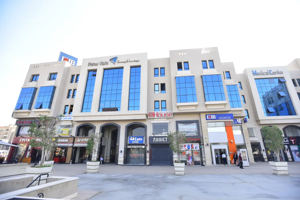 Prima Vista – Medical Office & Commercial Mall – منظر واسع من الساحة للواجهة ذات الأقواس مع المحلات والمطاعم والأشجار في أحواض
