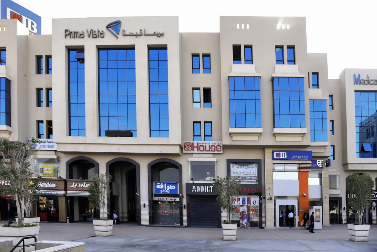 Prima Vista – Medical Office & Commercial Mall – الواجهة الرئيسية بنافذة زجاجية مركزية مرتفعة فوق رواق من المحلات