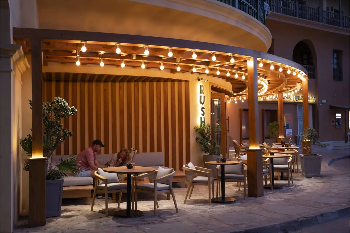 Rush – Sports Bar – رواد على تراس البرجولا بجوار جدار من الشرائح الخشبية ومقعد جلوس طويل