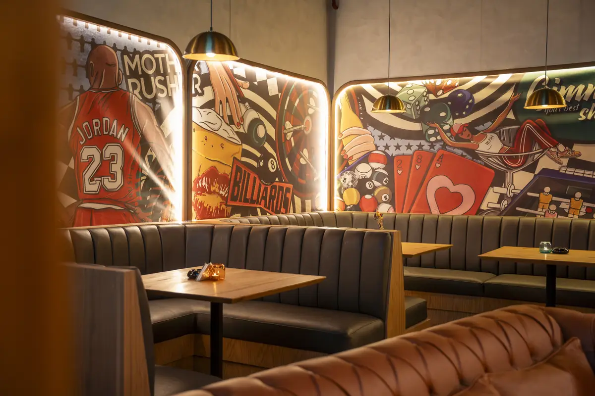 Rush – Sports Bar – مقصورات جلدية أسفل جداريات بوب آرت مضاءة من الخلف تصور كرة السلة والبلياردو وأوراق اللعب